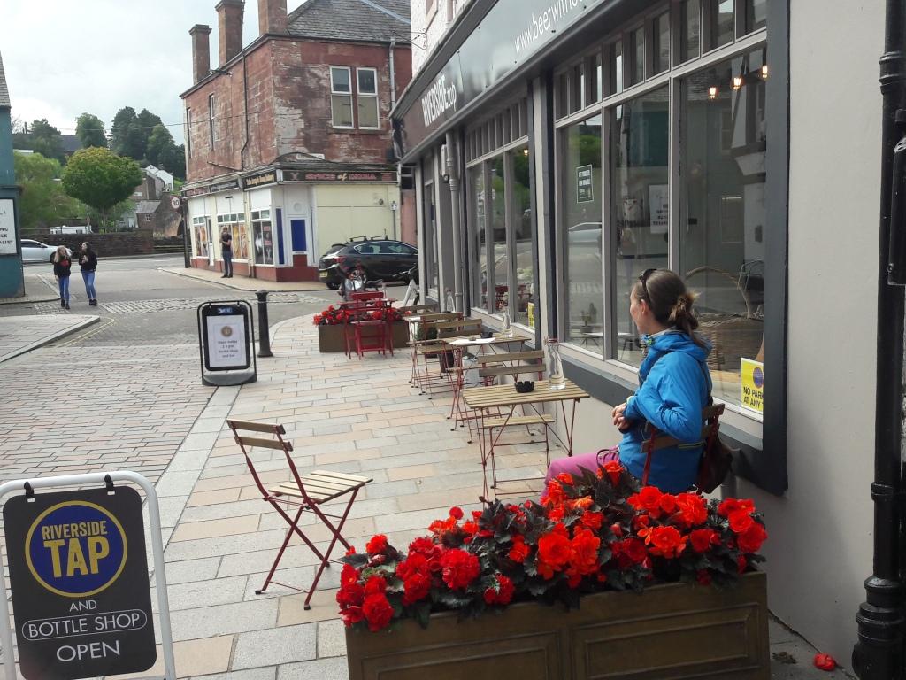 Woman sitting at tables outside a pub on the pedestrianised Vennel