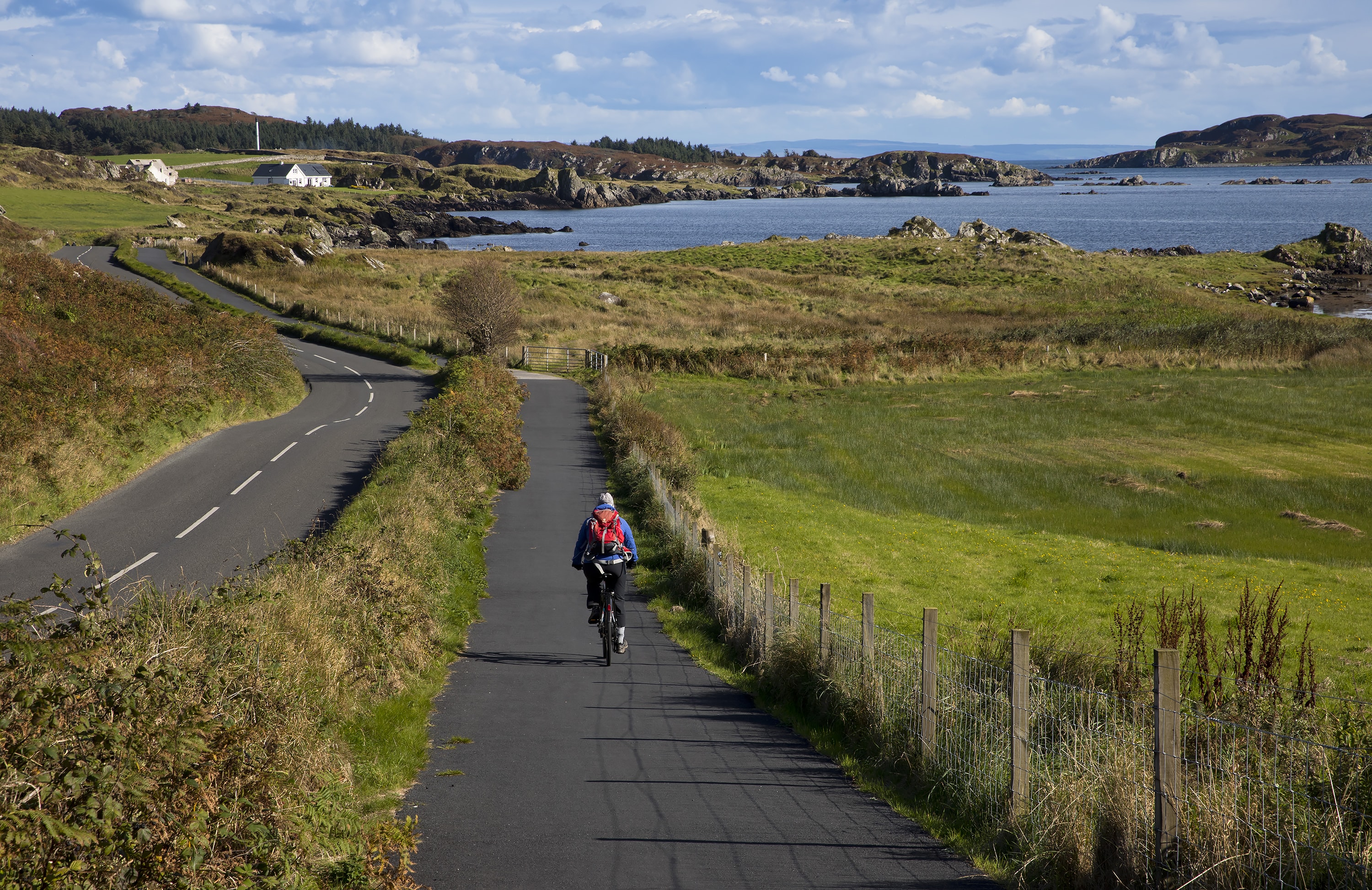 Islay three distilleries path, showing a cyclist separated from a rural road riding through coastal scenery