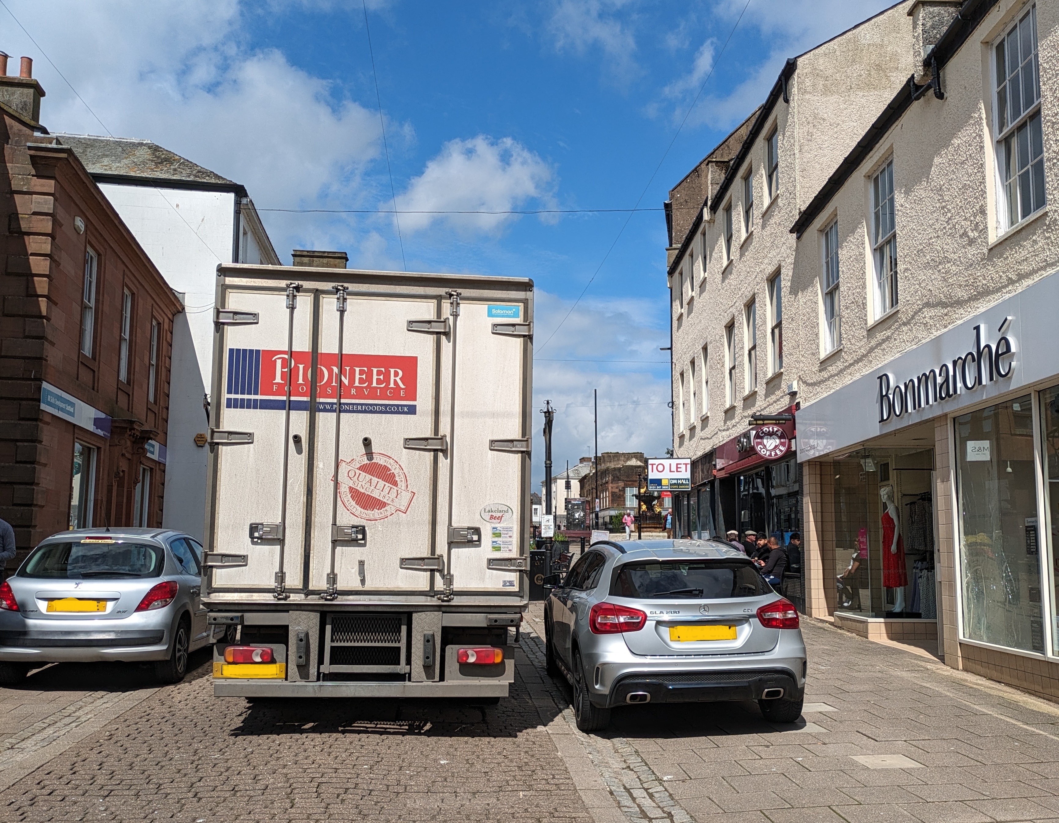 The high street with a lorry squeezing up the pedestrianised street between two parked cars